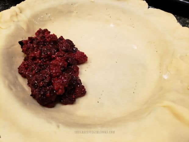 The pie crust pastry is pricked with the tines of a fork, then pie filling is added.