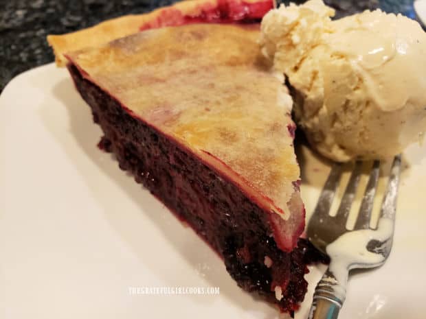 A slice of blackberry pie with a scoop of vanilla ice cream, served on a white plate.