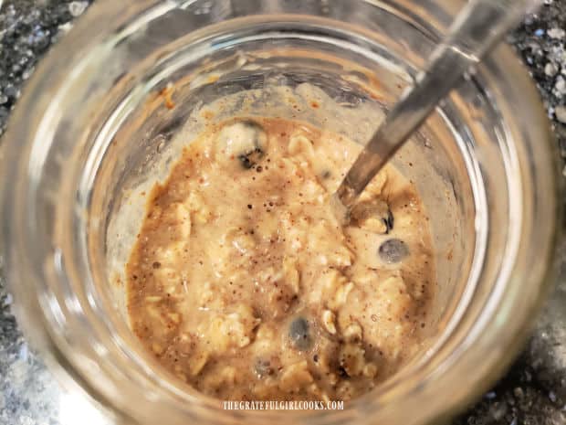 The overnight oats are mixed with fresh or frozen blueberries in the jar.