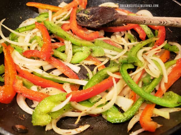 Red and green bell peppers, onions and spices are cooked in the skillet.