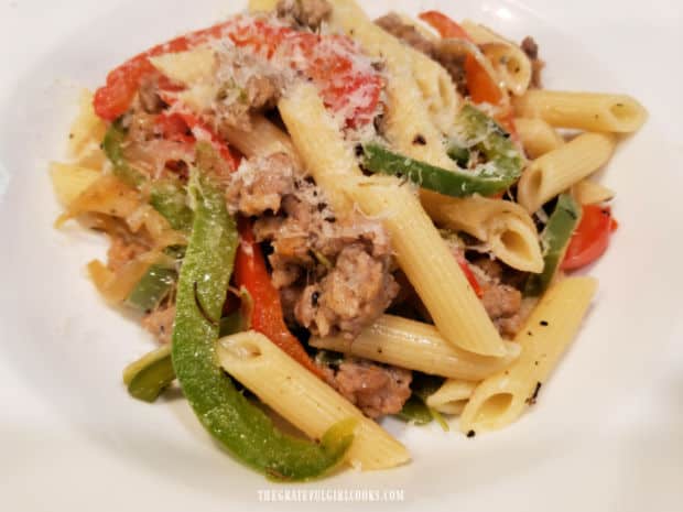 A portion of penne, sausage and peppers is topped with Parmesan cheese and served.