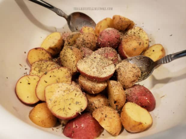 Olive oil and seasonings are added to the bowl of halved mini potatoes.