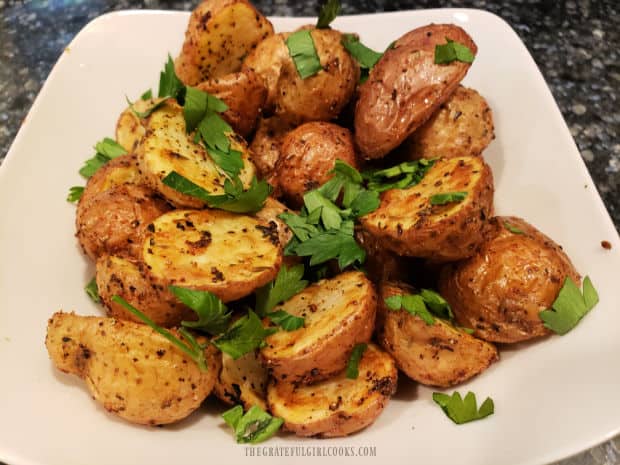 A white bowl of air fryer crispy mini potatoes garnished with parsley, ready to be eaten!