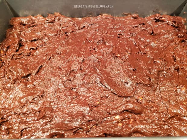 The batter for chocolate peanut butter brownies is spread into a greased cake pan.