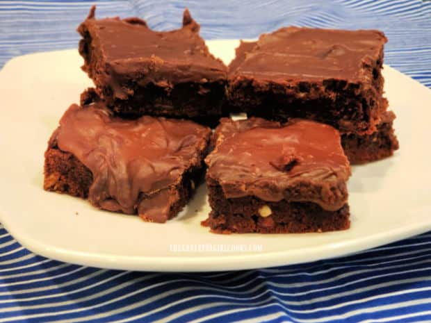 A white plate with several frosted chocolate peanut butter brownies on it.