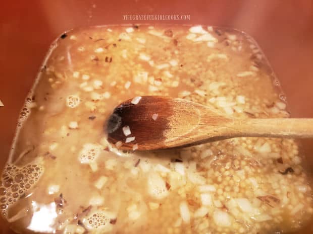 Chicken broth and spices are added to the onion and couscous in pan.