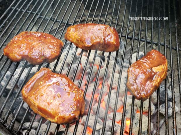 Four hoisin marinated pork chops are grilled over hot coals on a BBQ.