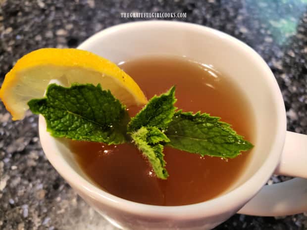 A mug of hot lemon mint tea, garnished with a mint sprig and lemon wedge, to serve.