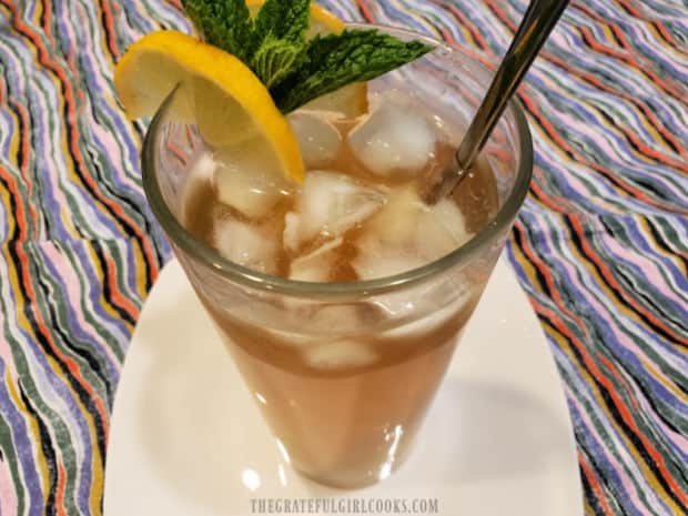 Iced cold lemon mint tea is garnished with a lemon wedge and mint sprig to serve.