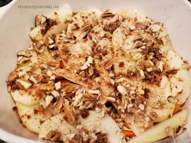 Pecans and cinnamon are sprinkled on a layer of apple slices in baking dish.