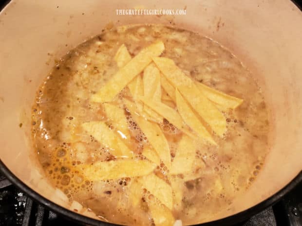 Unbaked corn tortilla strips are added to chicken broth and sauteed onion mixture in soup pan.