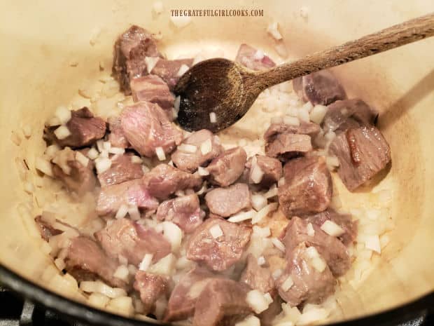 Cubes of stew meat and onions cooking in oil in large saucepan.