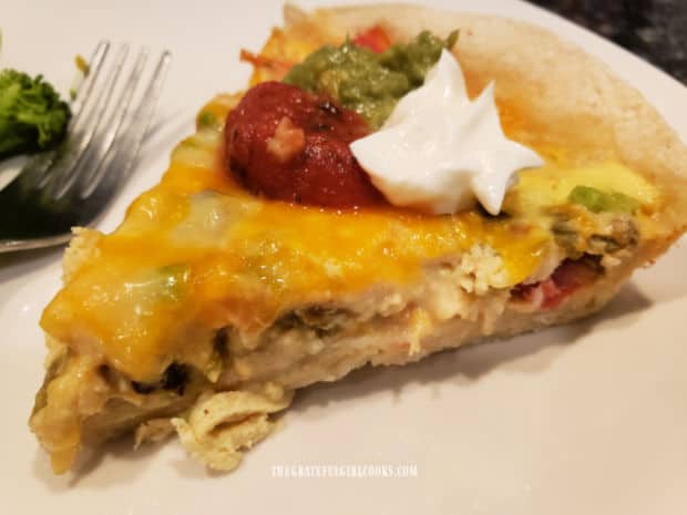 A slice of chicken enchilada quiche, with dollops of salsa, guacamole and sour cream.