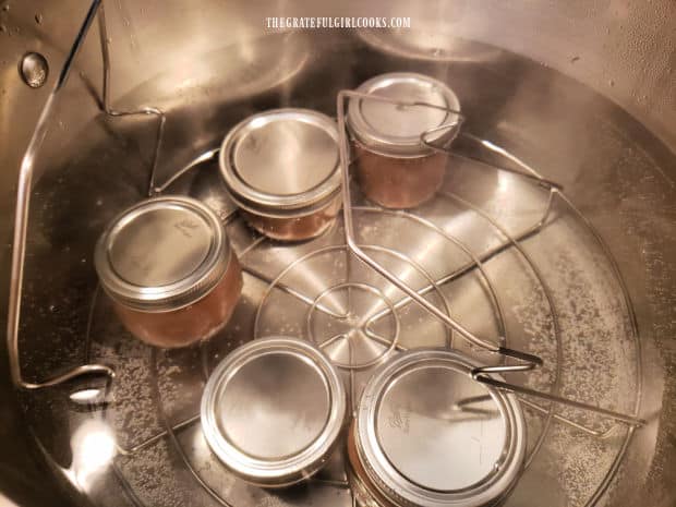 Jars of pear butter on canning rack are processed for 20 minutes in boiling water.