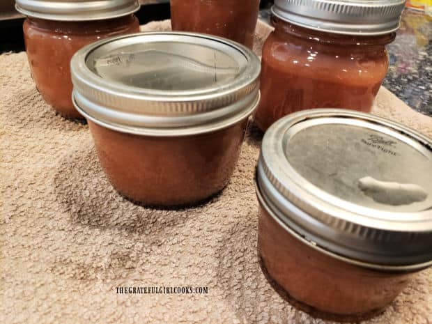 Several jars of canned pear butter cooling on a dish towel.
