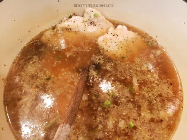 Lightly browned chicken breasts are added into soup to finish cooking.