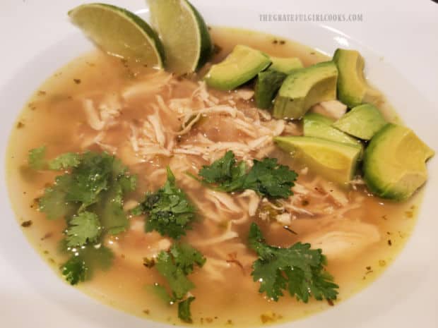 A bowl full of Southwestern chicken lime soup, topped with lime wedges, avocado and cilantro.