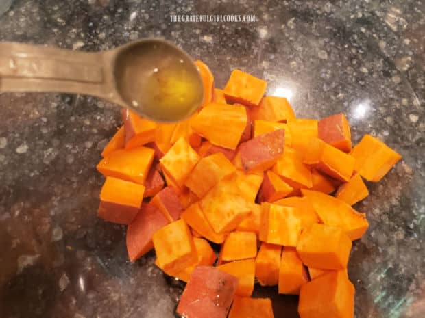 Olive oil is added to sweet potato cubes, then tossed to combine.