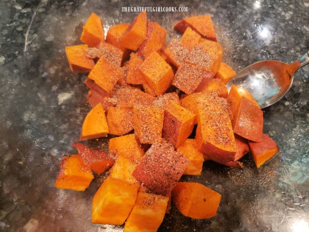 Seasoning mixture is added to oil-covered sweet potato cubes before cooking.