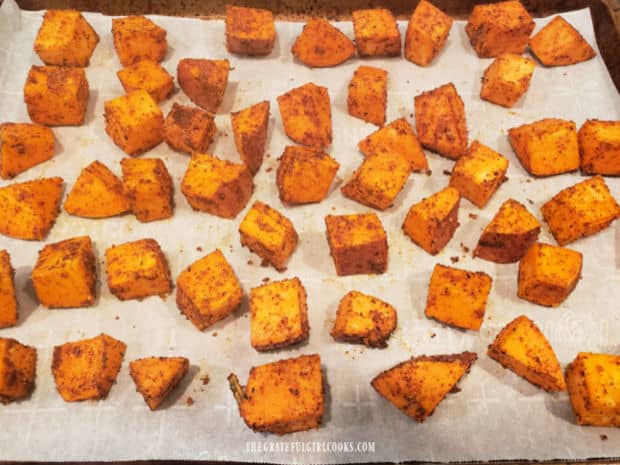 Single layer of spicy sweet potato bites on parchment paper, ready to bake.