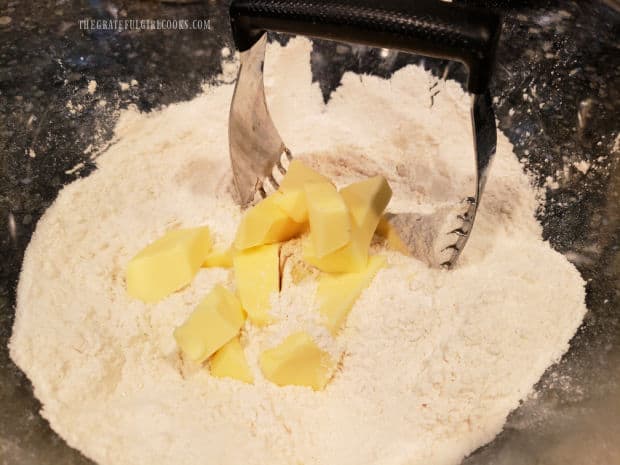 Cold butter is cut into the dry biscuit ingredients in a bowl.