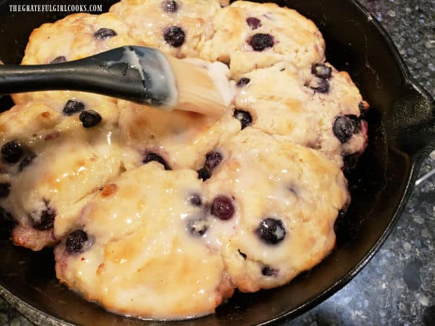 Brushing icing on the cooled vanilla glazed blueberry biscuits, after baking.