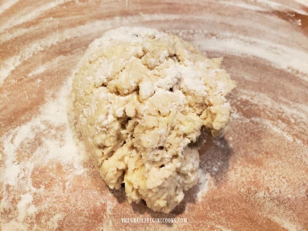 A shaggy ball of biscuit dough on a floured work surface before being flattened.