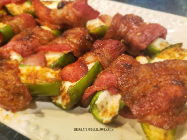 A white platter holding a dozen bacon wrapped jalapeño poppers, ready to be eaten.