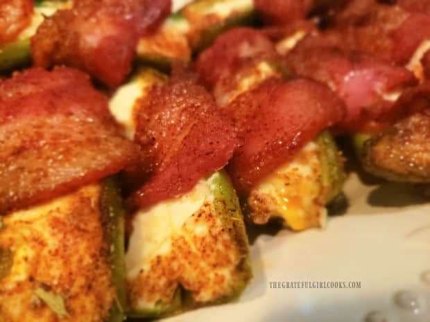 A close up photo of a couple of the bacon wrapped jalapeño poppers on serving plate.
