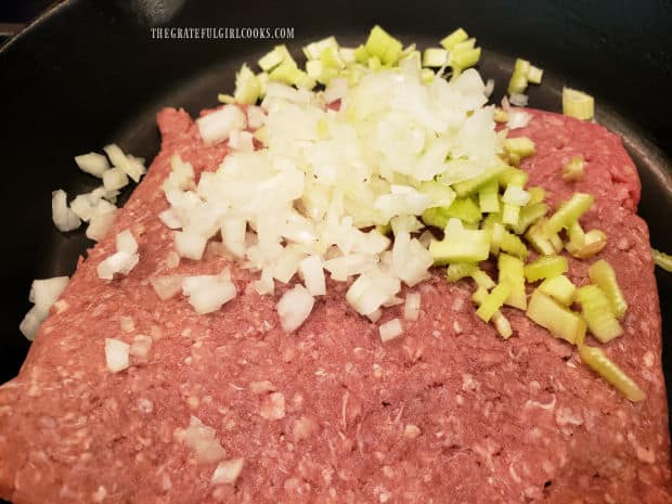 Ground beef is cooked in a skillet with chopped onions and celery.
