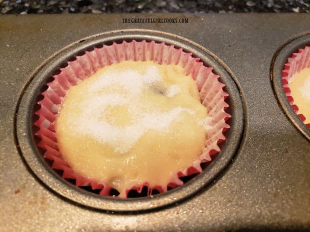 Muffin batter is added to cover jam, then muffin tops are sprinkled with sugar before baking.