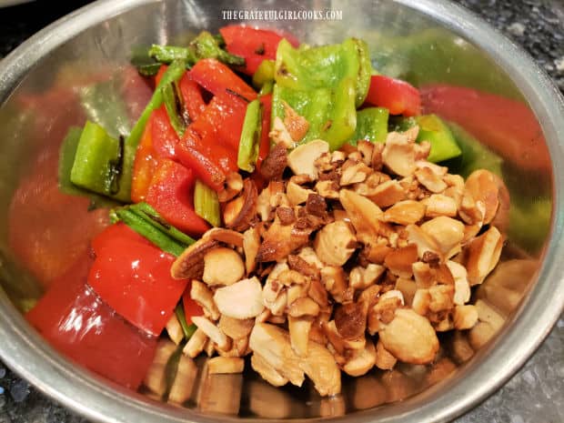 Cooked bell peppers, green onions and cashews rest in bowl before being added to chicken.