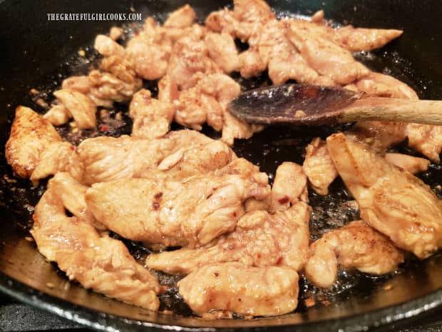 Marinated Szechuan chicken is quickly cooked in hot oil in a large black skillet.