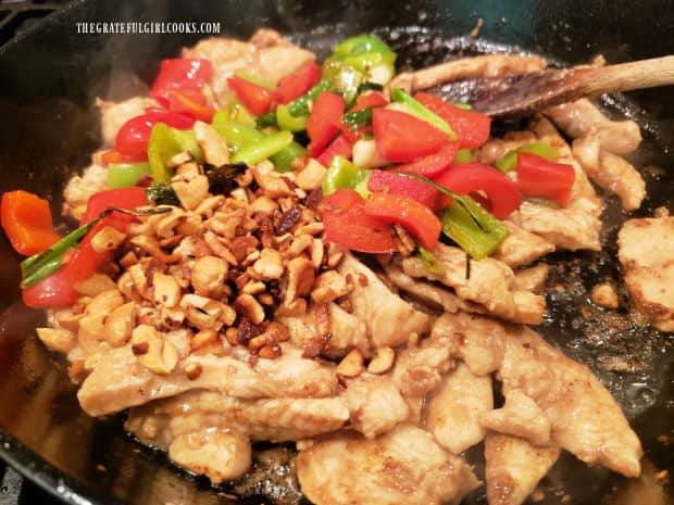 Green and red bell peppers, green onions and roasted cashews are added to the chicken in skillet.
