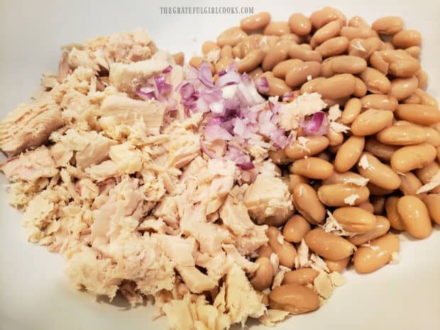 Rinsed, drained cannellini beans, red onion, and albacore tuna are combined in a large bowl.