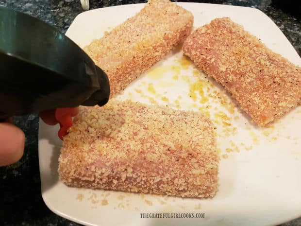 Panko coated fish fillets are spritzed with olive oil before being put into air fryer to cook.