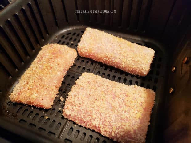 Three crusted mahi mahi fillets are placed in the air fryer basket to be cooked.