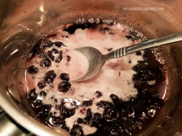 A water and cornstarch slurry is added to the blueberry jam and lemon juice in pan.