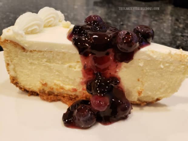 A slice of cheesecake is topped with some of the blueberry dessert sauce for serving.
