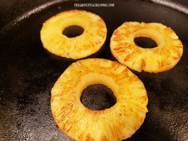 Canned pineapple rings are grilled in a skillet until golden brown on both sides.