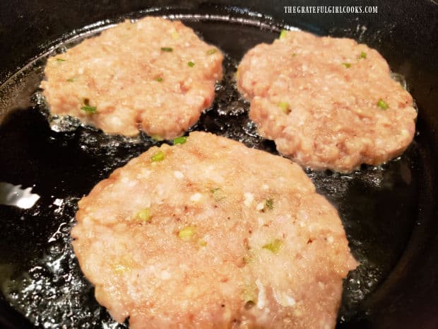 Chicken burger patties cooking in a large, cast iron skillet.