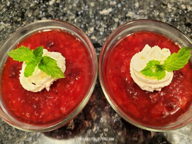 Two custard cups of jello salad, topped with whipped cream, mint and orange zest.