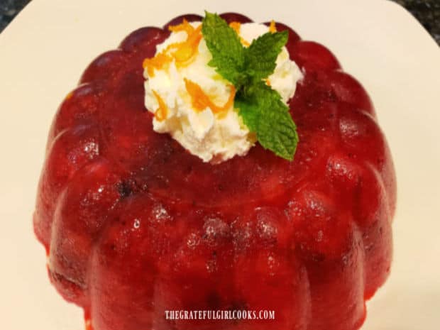 Cranberry Pineapple Jello Salad, out of plastic mold, topped with whipped cream, mint and orange zest.