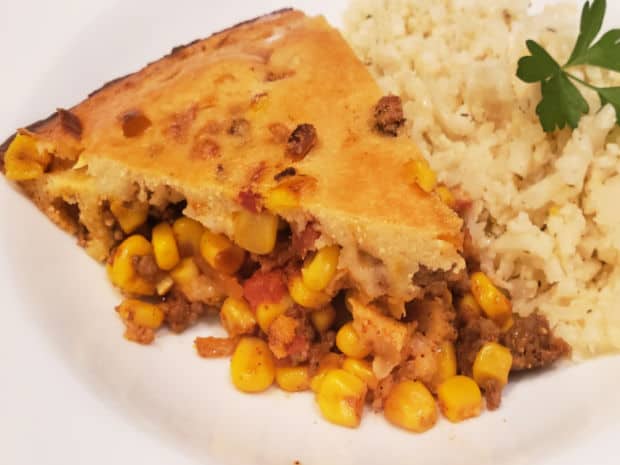 A slice of easy tamale pie on a white plate, with cauliflower rice on the side.
