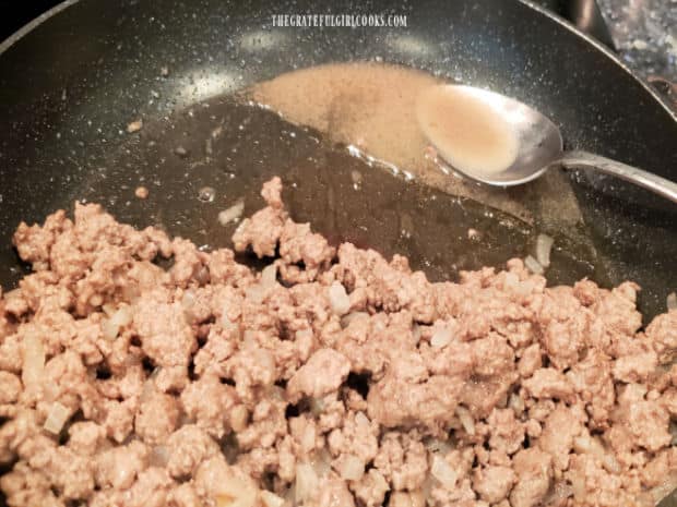 Accumulated grease is removed and discarded from the ground beef in the skillet.