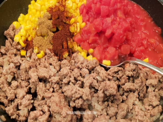 Corn, diced tomatoes and Mexican spices are added to the cooked meat in skillet.