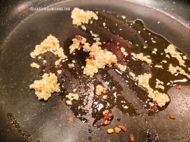 Minced garlic and red pepper flakes cook in hot oil in a large skillet.