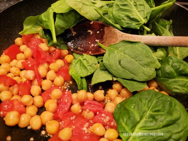 Baby spinach and salt are added to the garlic, tomato and chickpeas in skillet and cooked.