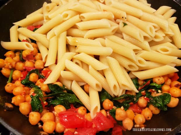 Cooked, drained penne pasta is added to the garlic and veggie sauce in skillet to combine.