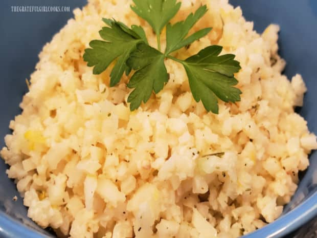 Lemon Garlic Cauliflower Rice is served in a blue bowl, and garnished with fresh parsley.